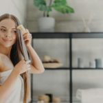 Attractive young woman smiles and enjoys her beauty, combes long straight hair after applying mask