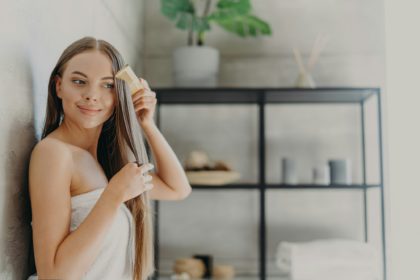 Attractive young woman smiles and enjoys her beauty, combes long straight hair after applying mask