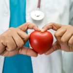 Doctor holding a red heart in hospital ward, healthy strong medical concept.