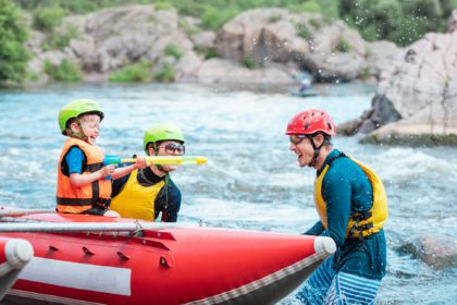 Family of three playing with water pistols near inflatable rowing catamaran