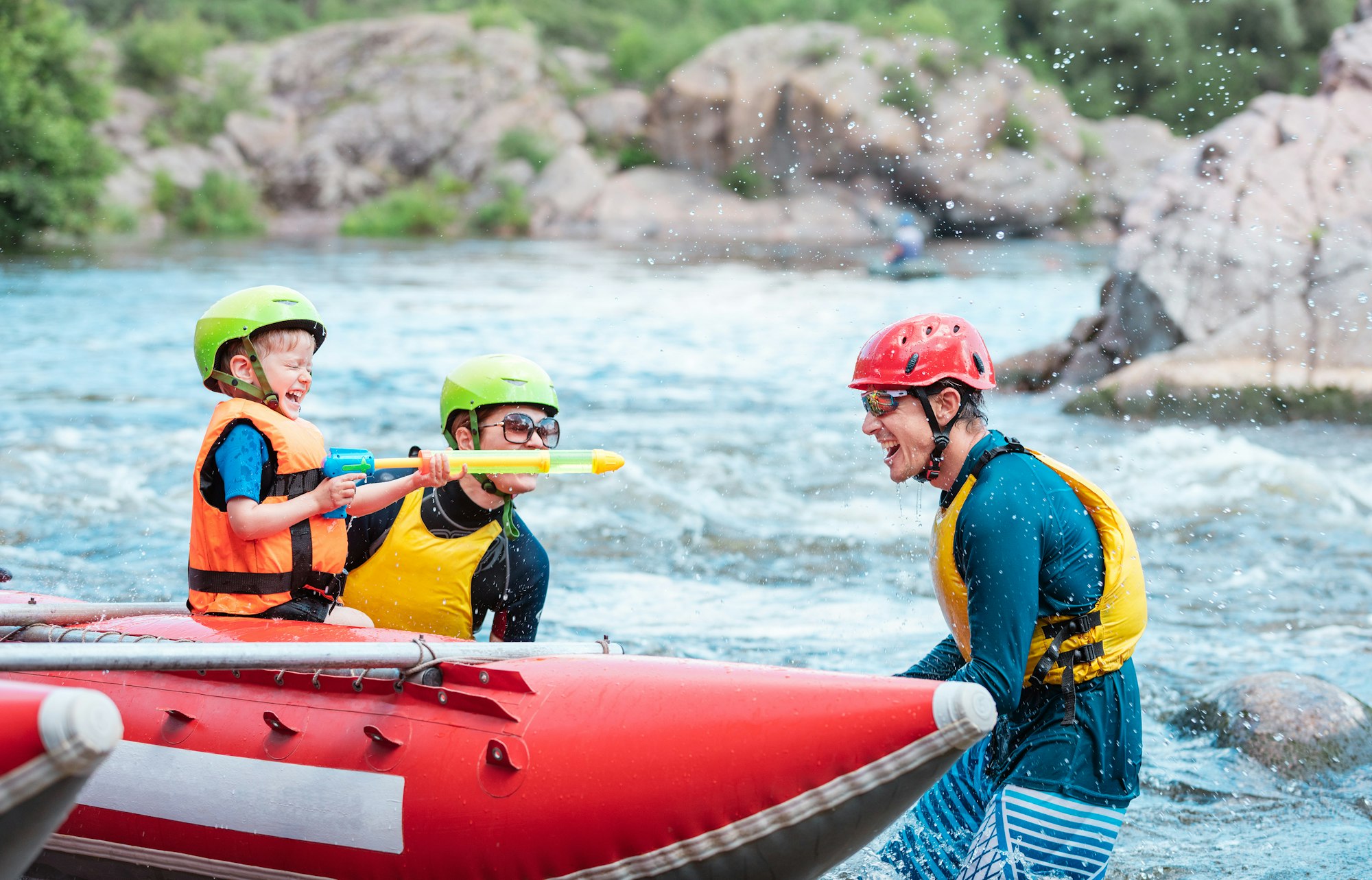 Family of three playing with water pistols near inflatable rowing catamaran