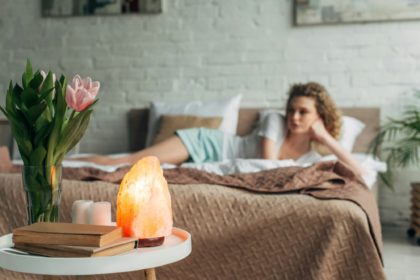 selective focus of girl resting in bedroom with Himalayan salt lamp, flowers and books